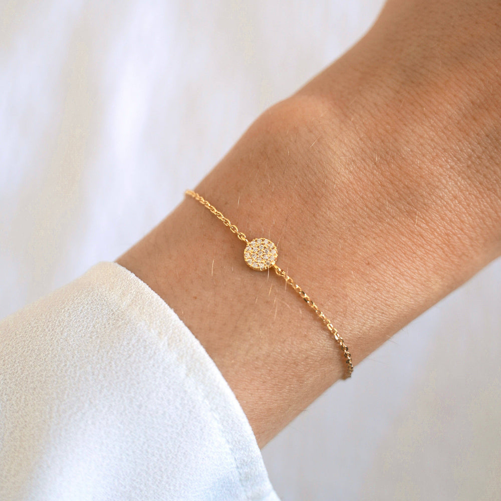 Gold necklace with a round, diamond-studded pendant on a white background