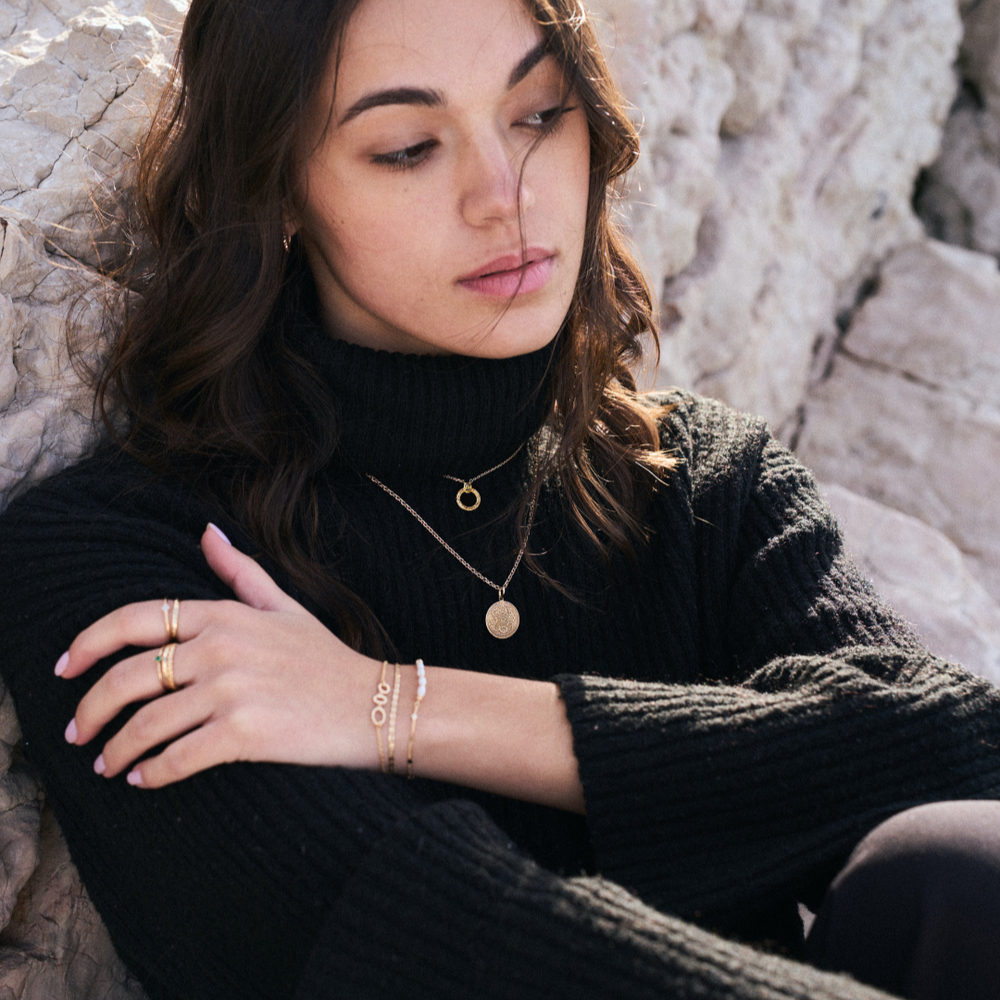 Gold necklace with a circular pendant on a white background