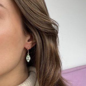 Close-up of a person wearing a silver earring with a clear gemstone.