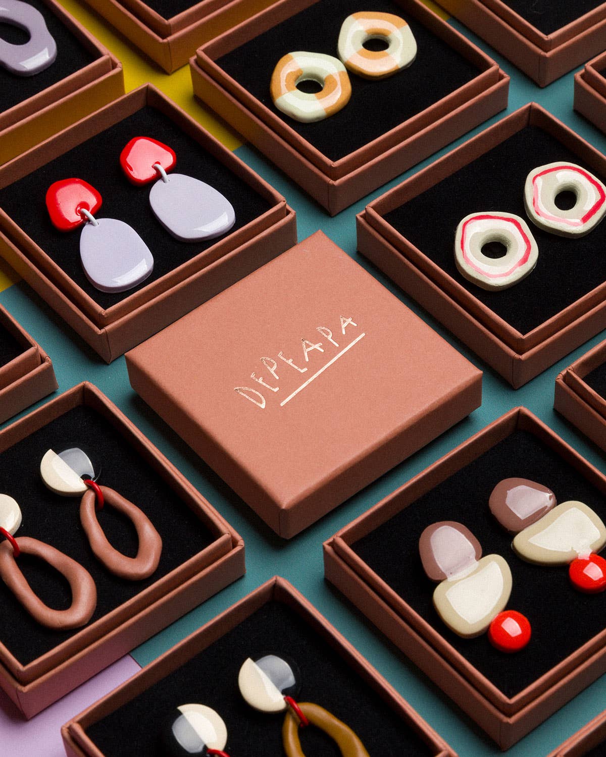 Colorful earrings in small brown boxes with a 'Diplada' box in the center.