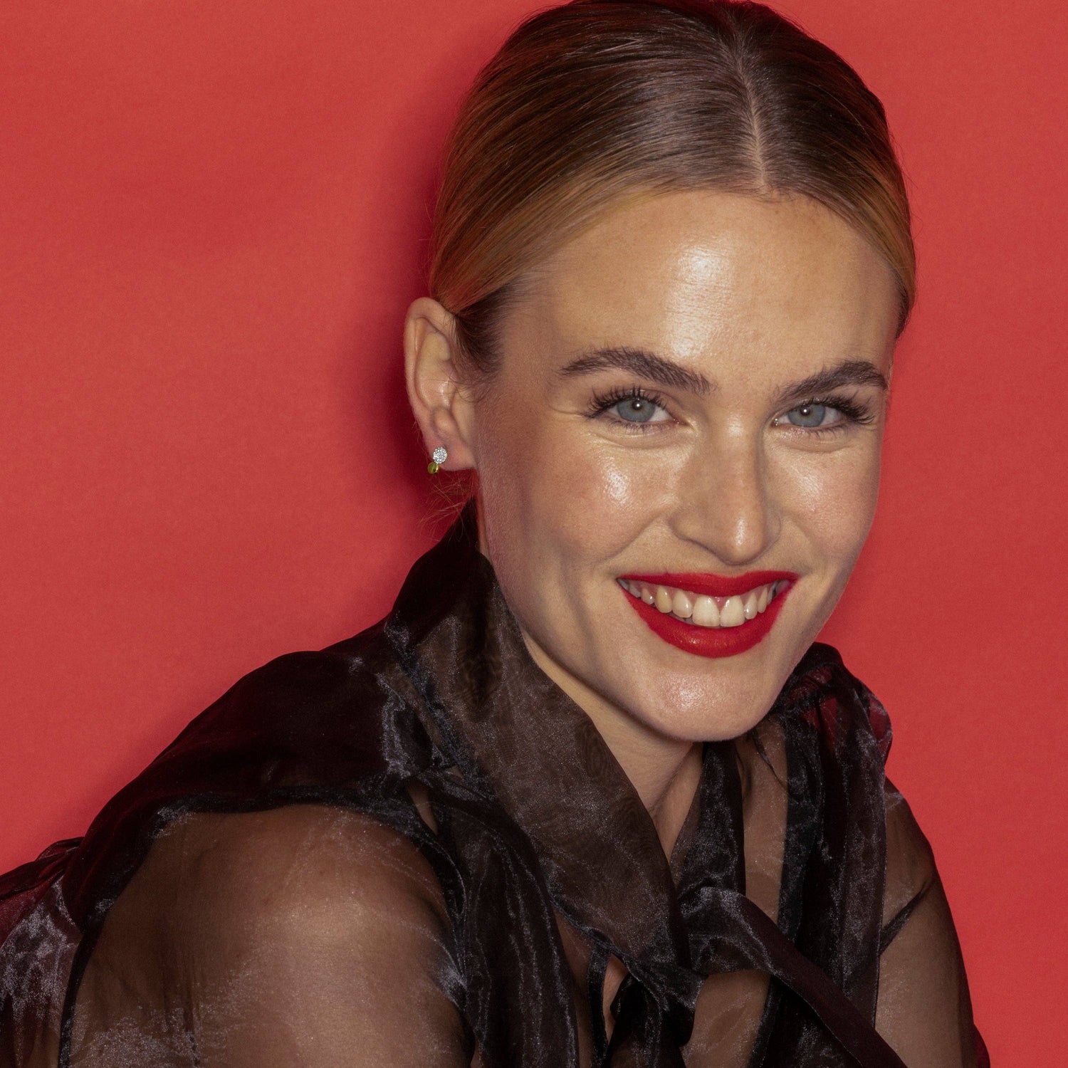 A close-up portrait of a smiling woman with blonde hair pulled back, wearing Beautifull Earrings