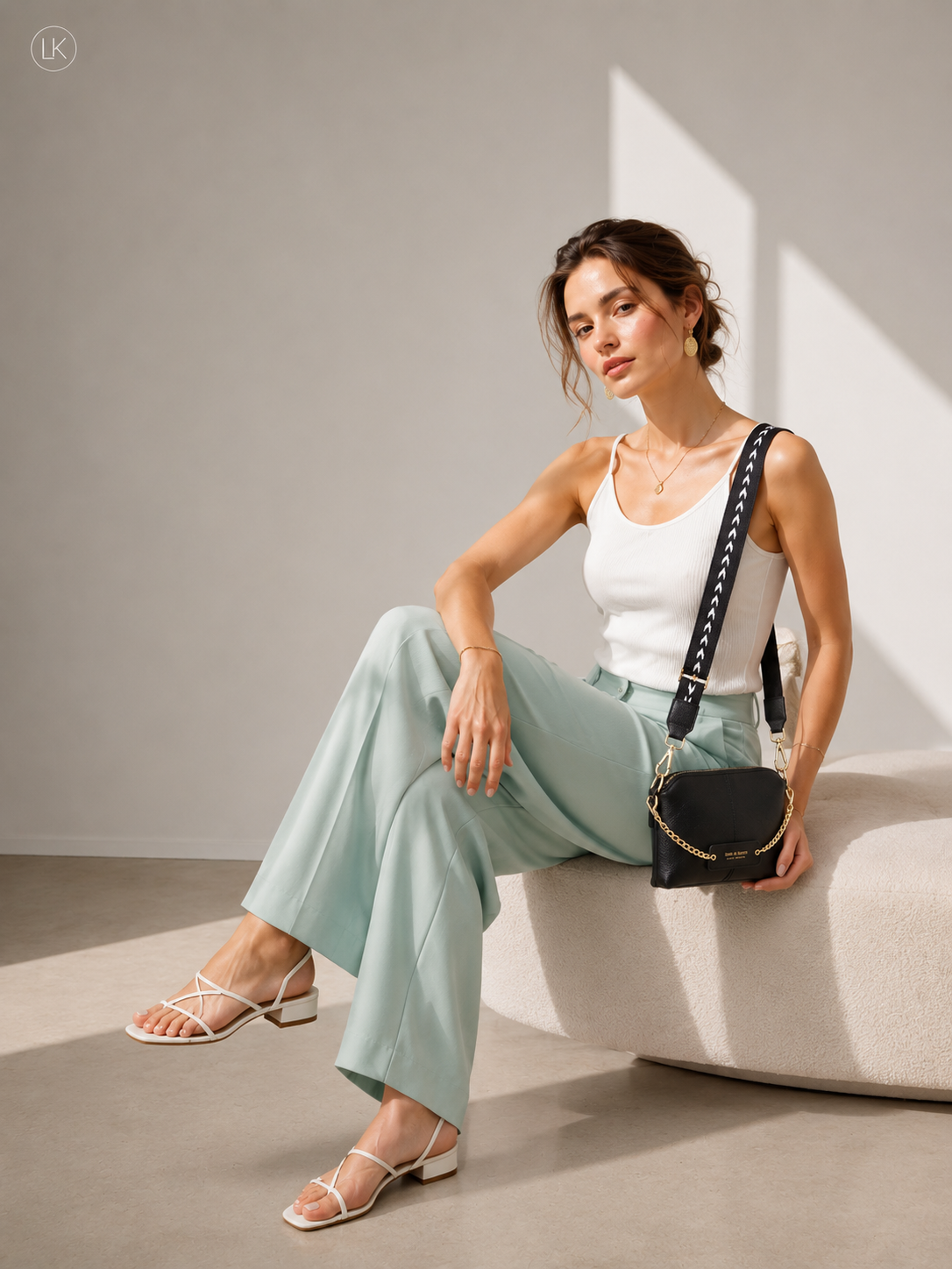 Black leather crossbody bag with gold chain detail and patterned strap worn by woman in white tank top and light green pants, part of Bags & More collection