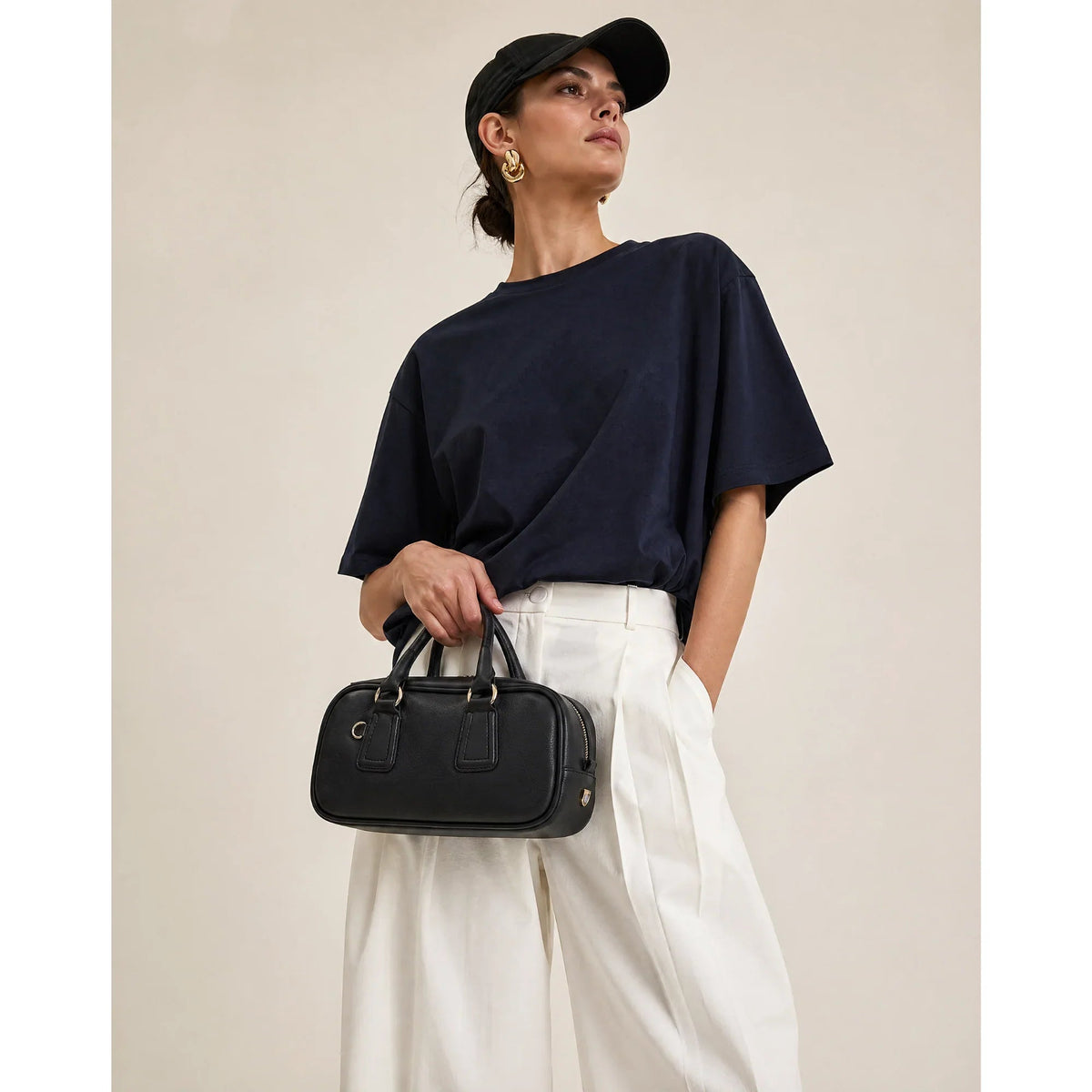 DuDu® black nappa leather handbag with gold hardware, clean rectangular shape, held by a model in navy top and white trousers