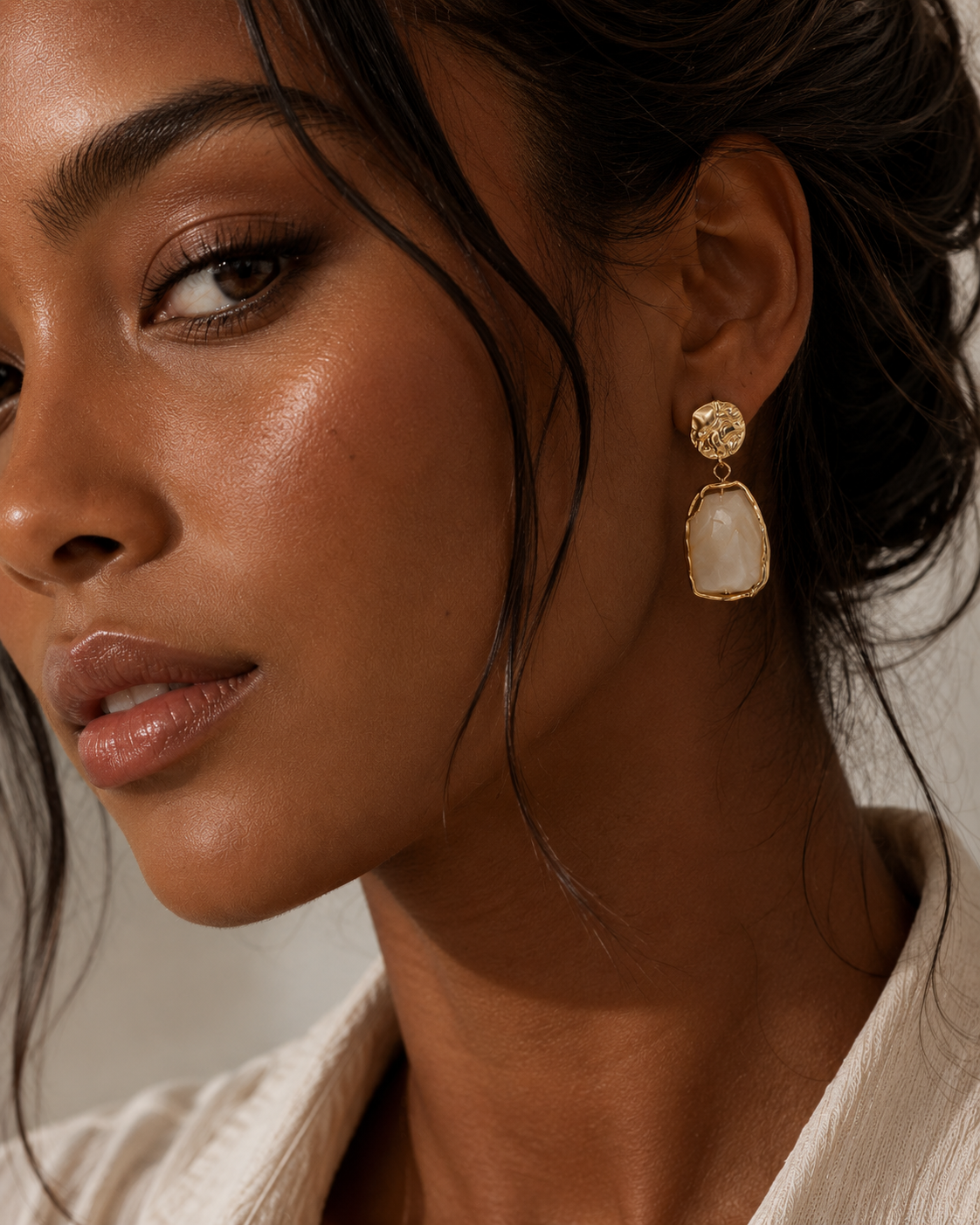 Earrings with gold plating featuring a textured round stud and a dangling irregular white stone pendant worn by a woman
