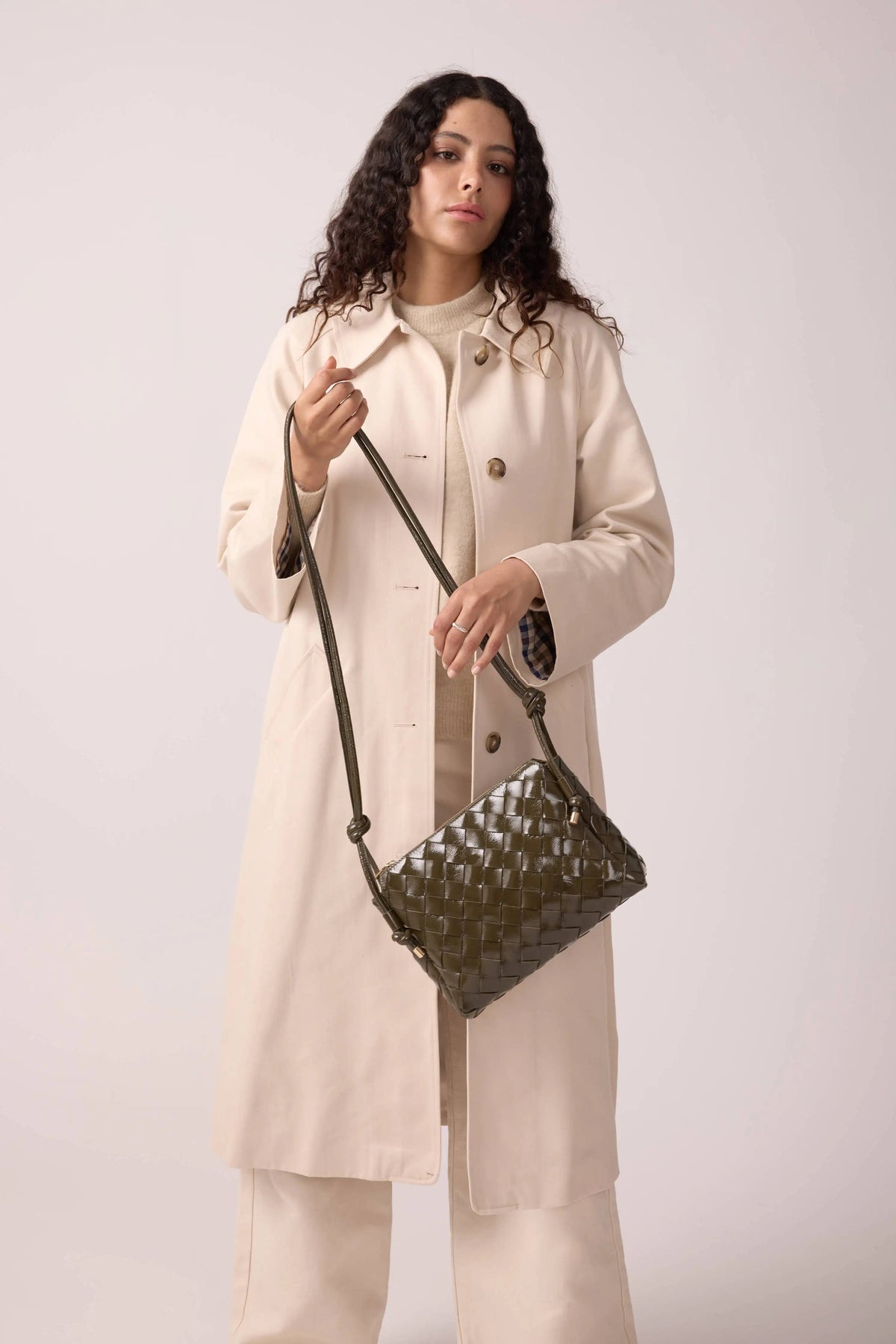 Maradji woven dark green leather crossbody bag with adjustable strap held by woman in beige coat and pants