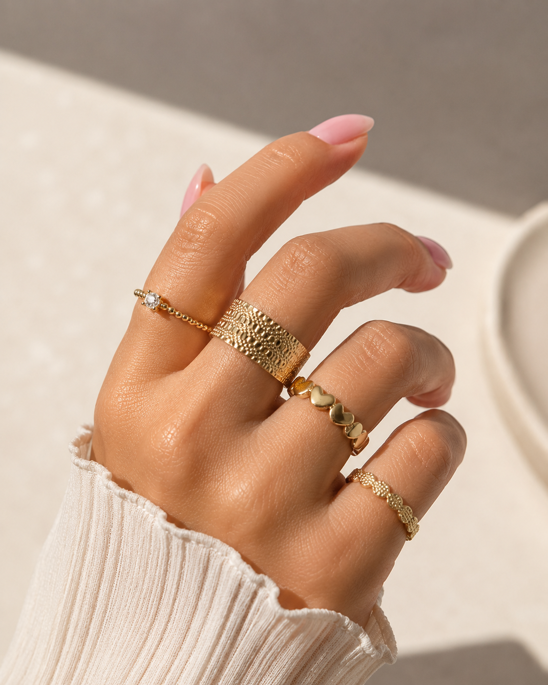 Ring set of four gold-tone rings on hand with different textured patterns including hearts and beaded design