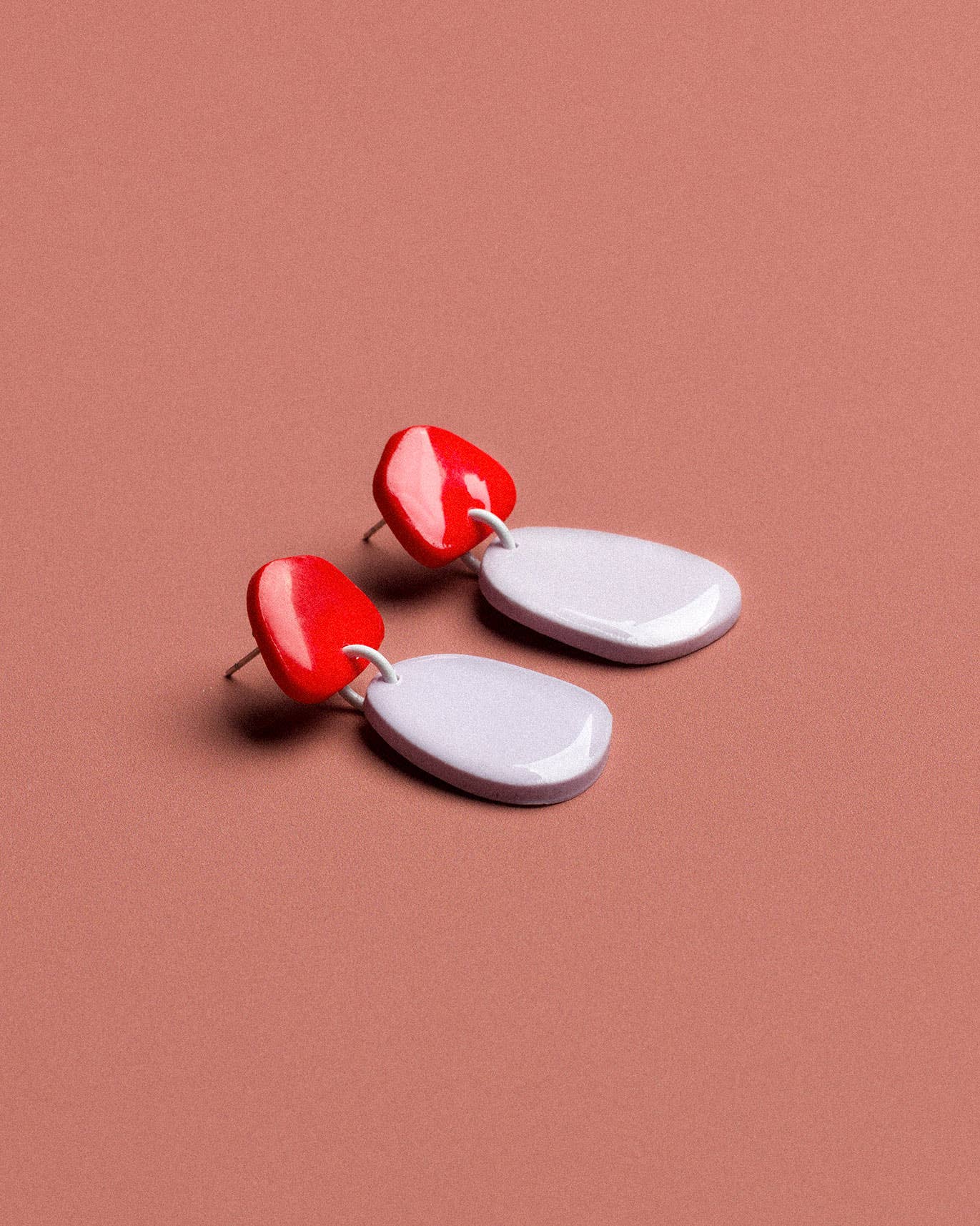Pair of earrings with red and white teardrop shapes on a brown background