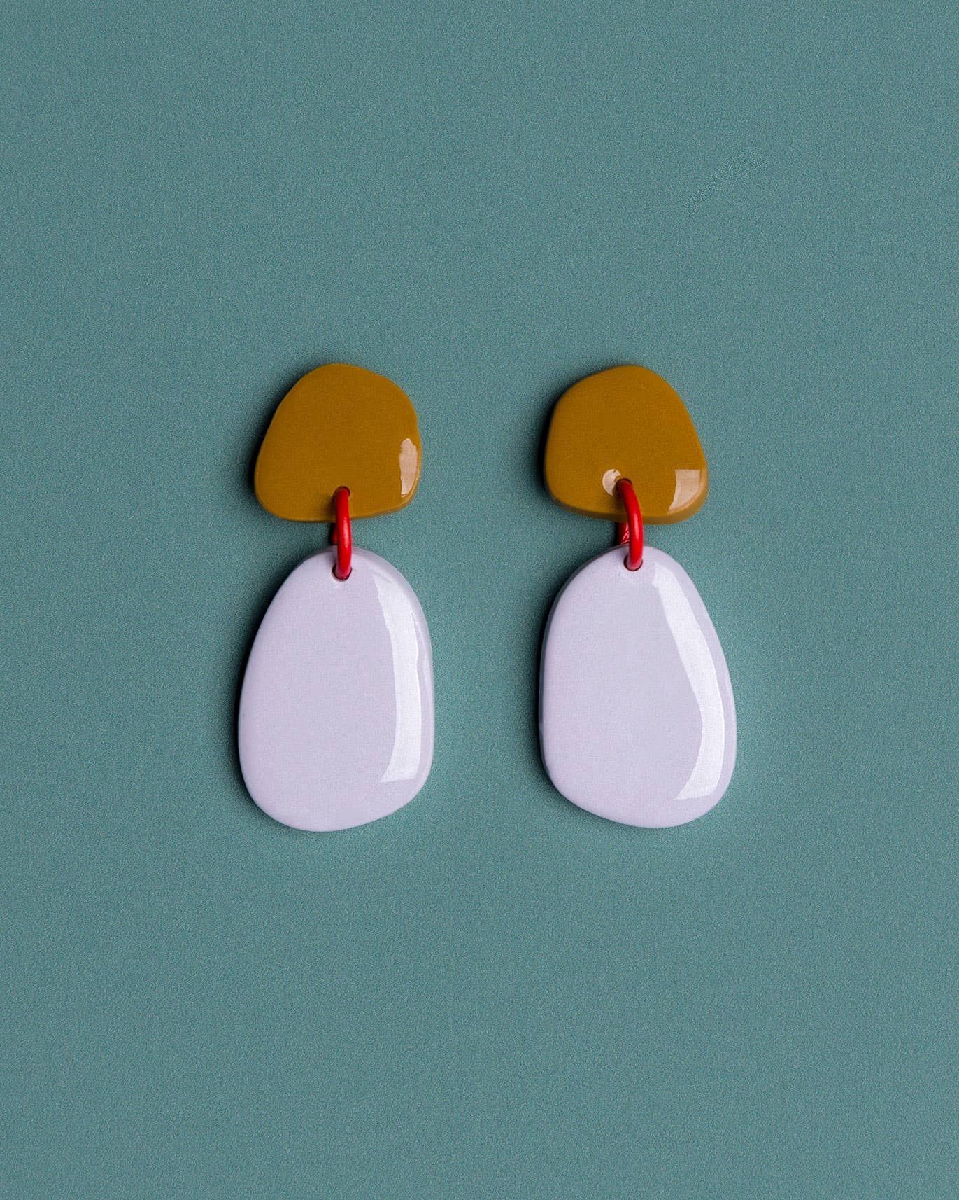 Pair of earrings with a mustard yellow top and white bottom on a teal background