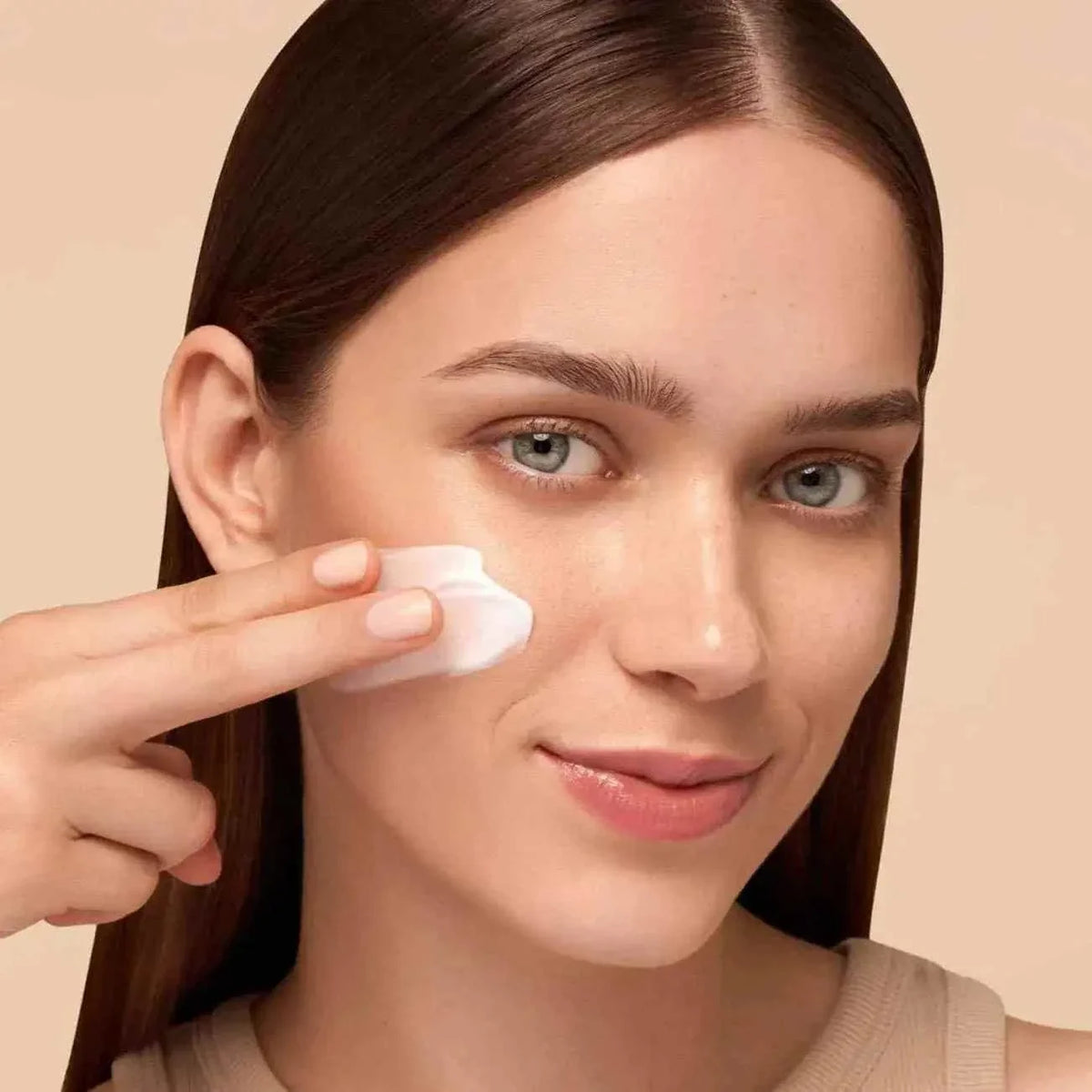 Woman applying white cream to her cheek demonstrating Care - Feel Intense - Day skincare routine for hydrated, firm skin