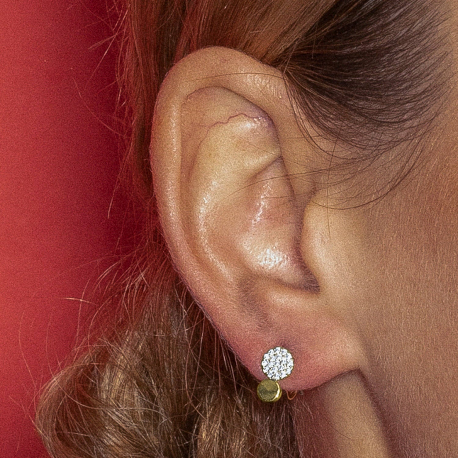  close-up of a person's ear wearing a small stud earring with a round pavé crystal top and a small gold ball charm