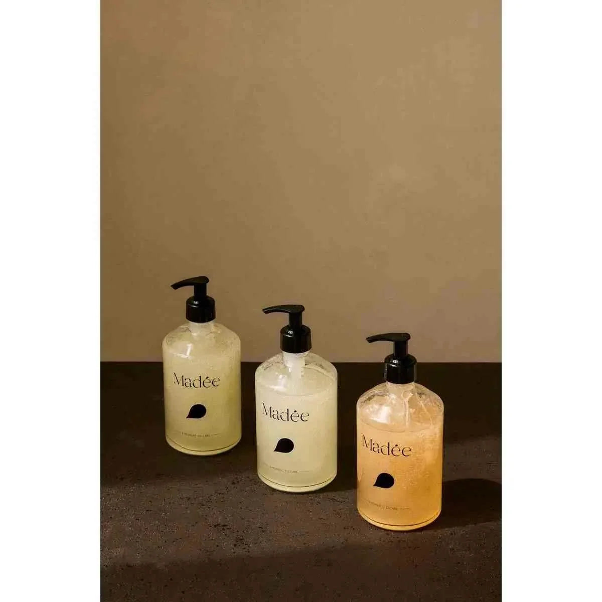 Madée Glass Hand Soap Set featuring three transparent glass bottles with black pumps containing pale yellow, creamy white, and amber liquid soaps