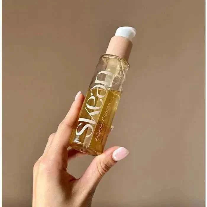 SkeanBeauty Essential Cleanser in a clear bottle with yellow liquid and beige pump held by hand