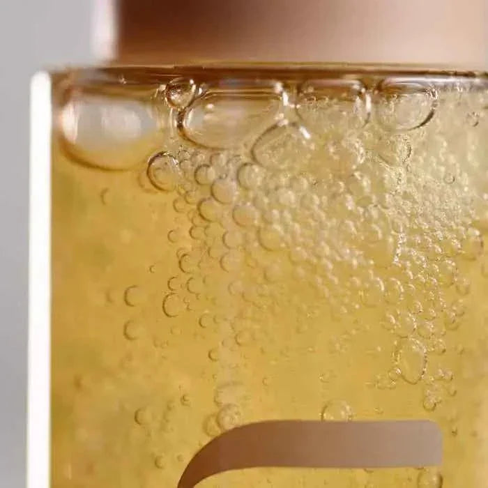 Close-up of translucent golden liquid with bubbles inside a clear container, representing SkeanBeauty Essential Cleanser
