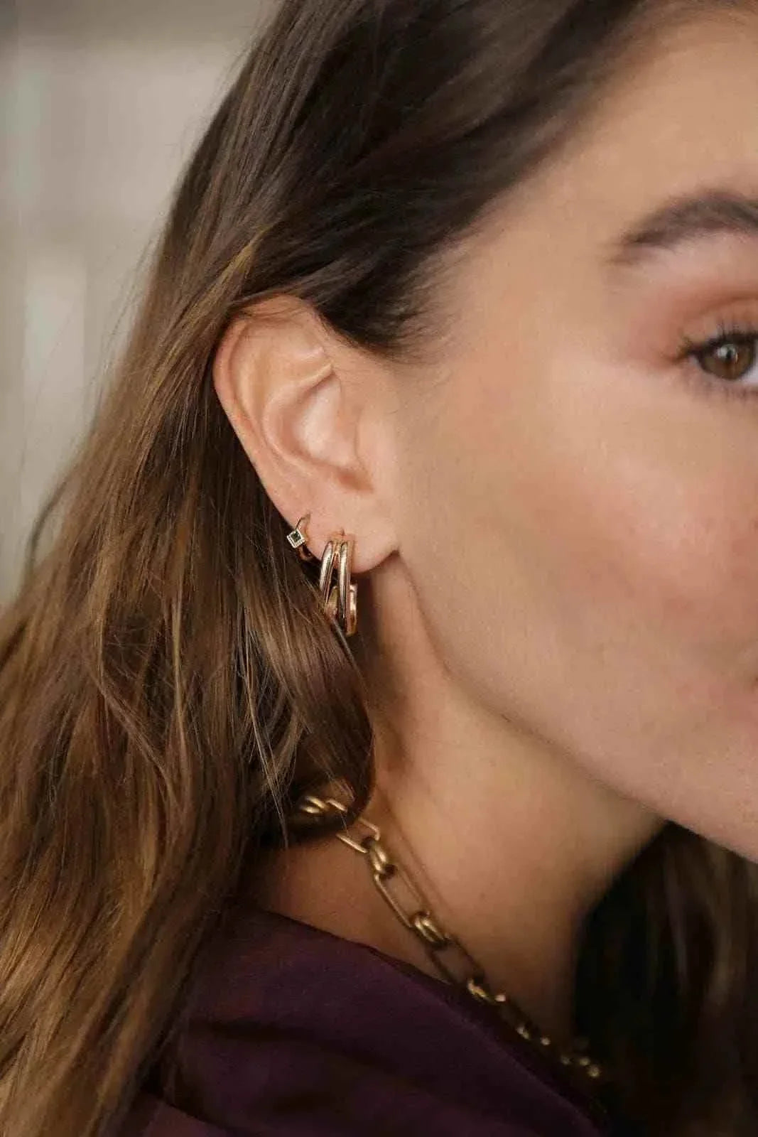 WAEKURA Mona earrings in gold-tone with a minimalist, elegant design worn on a woman's ear, paired with a gold chain necklace