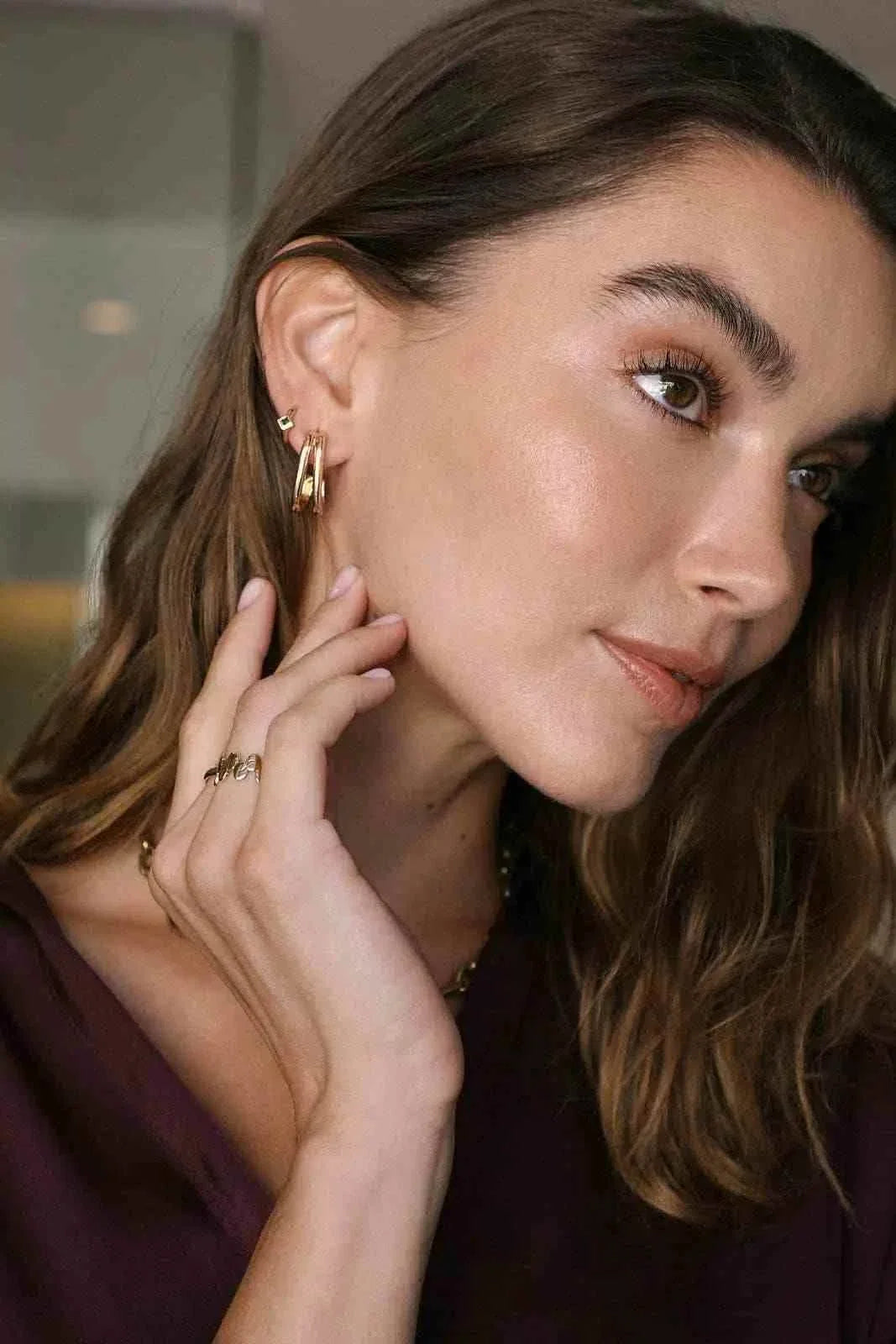 WAEKURA Mona earrings elegant gold-tone minimalist hoop design worn by woman with long brown hair